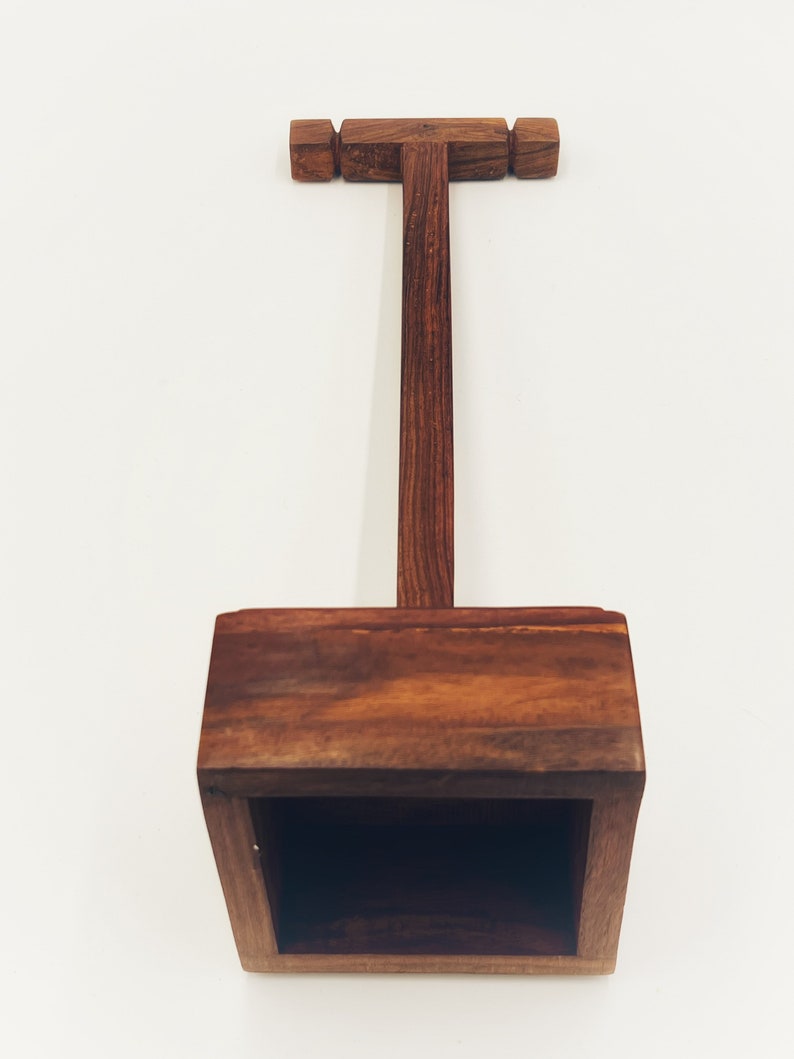 May include: A wooden headphone stand with a square base and a T-shaped top. The stand is made of dark brown wood.