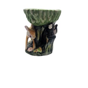 Puede incluir: Un cuenco de pedestal de cerámica con temática forestal. El cuenco tiene una parte superior verde texturizada, sostenida por una base de tronco de árbol. Un cervatillo y una pequeña figura se encuentran junto al tronco. La paleta de colores incluye tonos de marrón, verde y beige.