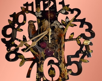 May include: A black resin clock shaped like a tree with gold-colored hands and Roman numeral hour markers. The clock face is filled with dried flowers and leaves.