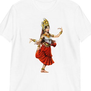 May include: A white t-shirt with a colorful illustration of a woman in a traditional Cambodian dance costume. She is wearing a red skirt, a white top, and a gold headdress. She is in a pose with her leg extended and her arms outstretched.