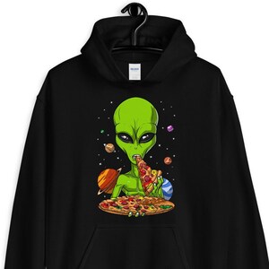 Puede incluir: Sudadera con capucha negra con un extraterrestre verde comiendo pizza en el espacio. El extraterrestre está rodeado de planetas y estrellas.