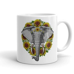 Op de afbeelding: Witte keramische mok met een afbeelding van een grijze olifant die een bloemenkrans draagt. De olifant is omringd door gele zonnebloemen en witte madeliefjes.