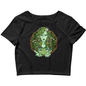 Puede incluir: Camiseta negra de corte corto con un gr&aacute;fico de una mujer con piel y cabello verdes, rodeada de hojas y flores. Ella sostiene dos colibr&iacute;es en sus manos.