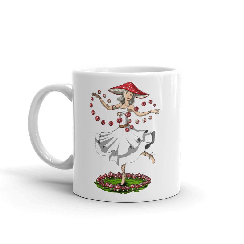Może przedstawiać: Biały kubek ceramiczny z kolorową ilustracją kobiety w czerwono-białym kapeluszu i sukience w kształcie grzyba. Jest otoczona czerwonymi i białymi grzybami i tańczy.