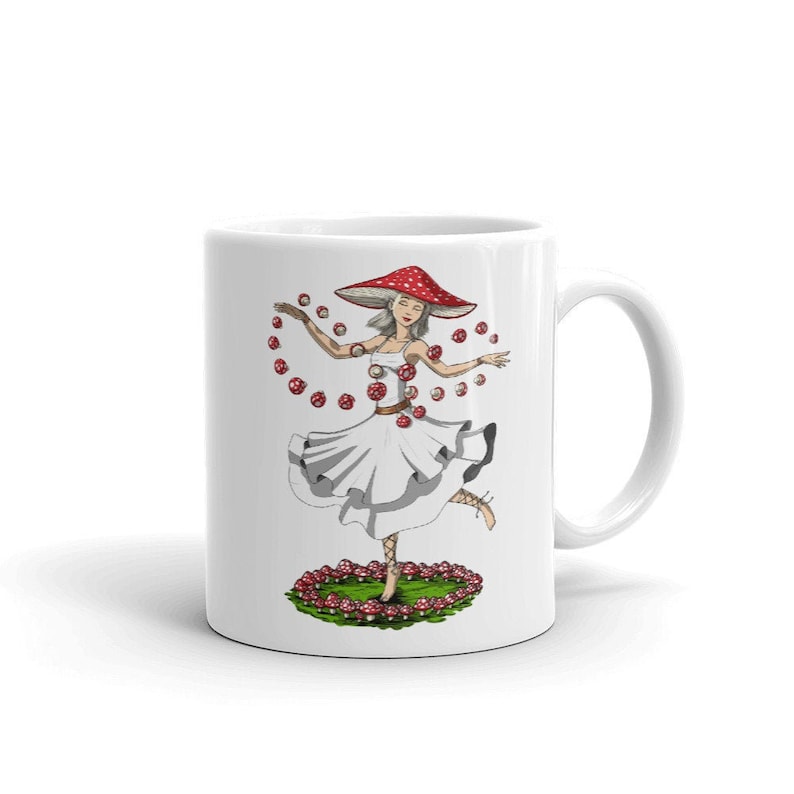 Może przedstawiać: Biały kubek ceramiczny z kolorową ilustracją kobiety w czerwono-białym kapeluszu w kształcie grzyba i białej sukience. Jest otoczona czerwonymi i białymi grzybami i tańczy z wyciągniętymi rękami.