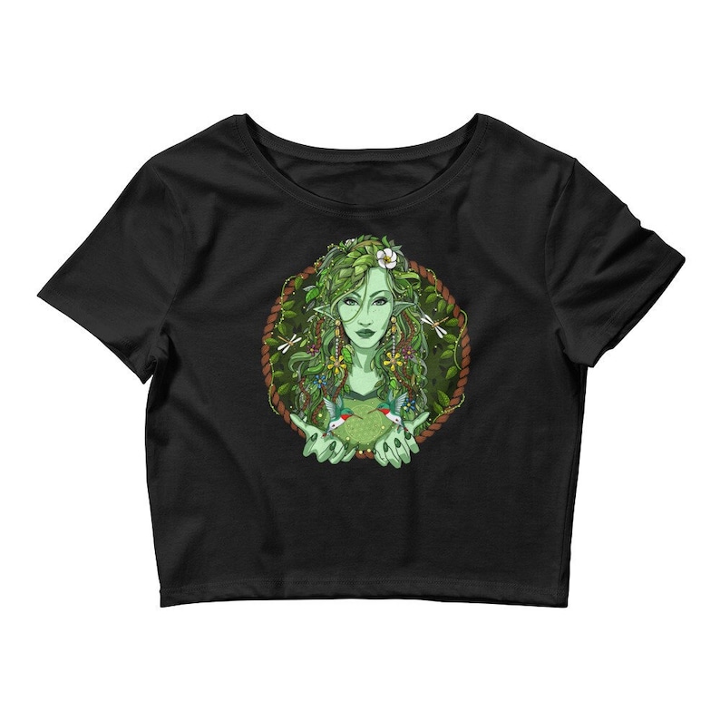 Puede incluir: Camiseta negra de corte corto con un gr&aacute;fico de una mujer con piel y cabello verdes, rodeada de hojas y flores. Ella sostiene dos colibr&iacute;es en sus manos.