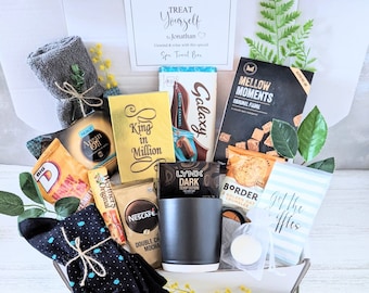 Puede incluir: Una caja de regalo llena de diversos artículos, que incluyen un par de calcetines grises, un par de calcetines negros, una taza, una barra de chocolate, una bolsa de chispas de chocolate, una bolsa de fudge, una bolsa de granola, una bolsa de café, un pequeño frasco de loción y una tarjeta que dice "Date un capricho".