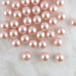 Puede incluir: Una colección de cuentas de perlas de color rosa pálido, esparcidas sobre una superficie blanca.