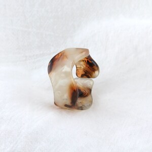 May include: A brown and white tortoiseshell hair clip with a unique curved shape.