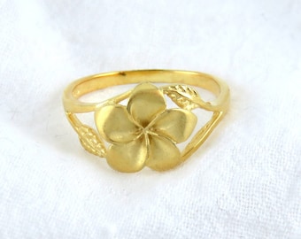May include: A gold ring with a flower design. The flower is a plumeria, a tropical flower with five petals.