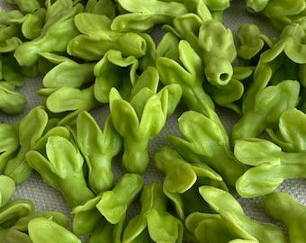 May include: A pile of small, light green, flower-shaped craft supplies. Each piece has a three-petal design and a small stem. The objects are scattered across a neutral-colored surface, suggesting a crafting or decorative theme.