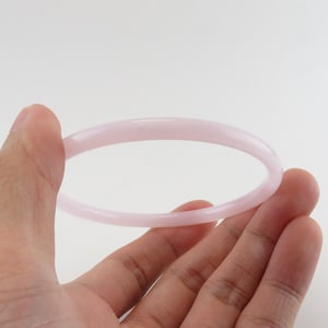 May include: A pale pink bangle bracelet made of smooth, polished stone.