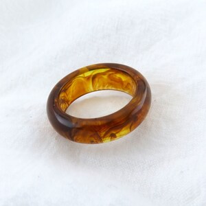 May include: A brown and yellow resin ring with a swirl pattern.