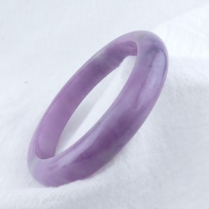 May include: A lavender jade bangle bracelet. The bangle is smooth and polished, with a light purple hue.
