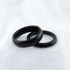 May include: Two black rings, one slightly larger than the other, are stacked on top of each other on a white surface.
