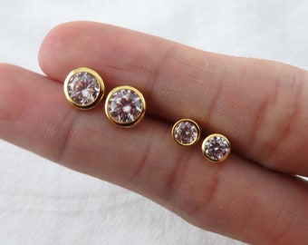 May include: Three pairs of gold stud earrings with clear round stones. The earrings are arranged in order of size, with the largest pair on the left and the smallest pair on the right.