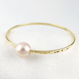 May include: A gold bangle bracelet with a single, light pink pearl charm.