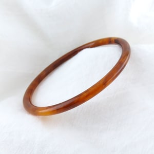 May include: A brown tortoiseshell bangle bracelet. The bracelet is made of a smooth, glossy material and has a simple, elegant design.