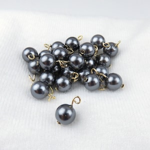 May include: A pile of gray pearl beads with gold wire loops. The beads are scattered on a white surface.