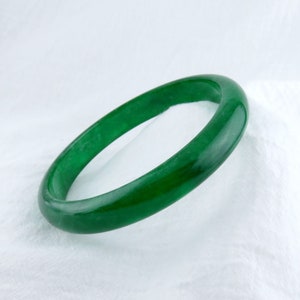 May include: A green jade bangle bracelet. The bangle is smooth and polished.