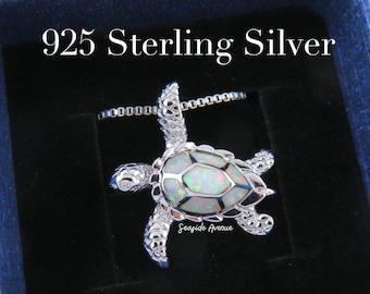 May include: A silver turtle pendant with an iridescent white opal shell. The pendant is on a silver chain and is in a blue velvet box. The box has the text "925 Sterling Silver" on the top.