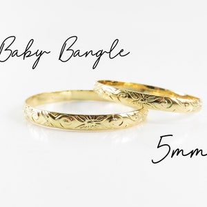 May include: Two gold-colored baby bangles with a floral design. The bangles are 5mm wide.