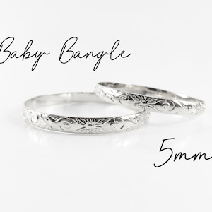 May include: Two silver baby bangles with a floral design. The bangles are 5mm wide.
