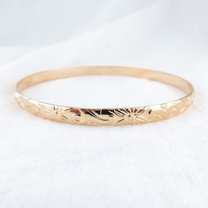 May include: A gold bangle bracelet with a floral design. The bracelet is smooth and shiny.
