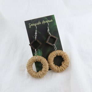 May include: A pair of earrings with a woven circle design and a small wooden square dangle. The earrings are on a card that says "Seaside Avenue".