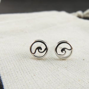 May include: A pair of silver stud earrings with a wave design. The earrings are circular and have a cutout wave shape in the center.