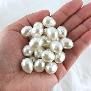 May include: A pile of large, white, faux pearl beads in a person's hand.