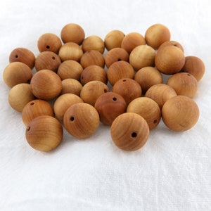 May include: A pile of natural wood beads, each with a hole drilled through the centre. The beads are a light brown colour and have a smooth, polished finish.