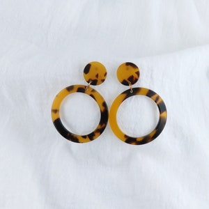 May include: A pair of brown and black tortoise shell hoop earrings with a smaller round disc at the top of each hoop.