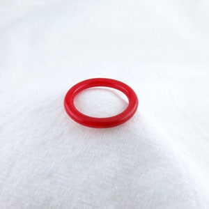May include: A simple red bangle bracelet made of smooth, polished plastic.