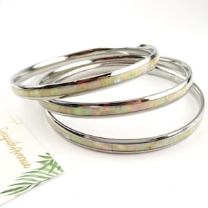 May include: Three silver bangles with a white opal inlay. The bangles are stacked on top of each other.