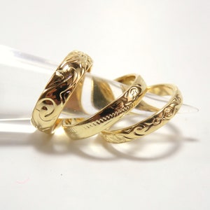 May include: Three gold rings with intricate engraved designs. The rings are stacked on top of each other.