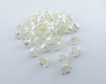 May include: A pile of off-white plastic flower embellishments with a pearl-like finish. The flower embellishments are in the shape of a bell with five petals.