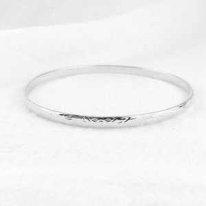 May include: A silver bangle bracelet with a delicate etched design.