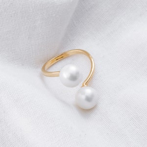 May include: A gold ring with two white pearls. The ring is designed to be worn on the knuckle.
