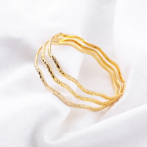 May include: Three gold-toned bangles with a hammered texture. The bangles are stacked on top of each other.