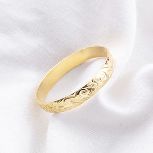 May include: A gold bangle bracelet with a floral design.