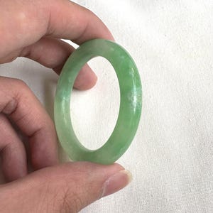 May include: A green jade bangle bracelet. The bangle is smooth and polished, with a light green colour.