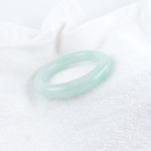 May include: A light green jade bangle bracelet. The bracelet is smooth and polished.