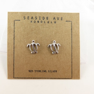 May include: A pair of sterling silver turtle stud earrings on a brown card with the text "Seashore Ave Honolulu" and "925 Sterling Silver".