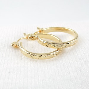 May include: A pair of gold hoop earrings with a floral design. The earrings are made of a smooth, shiny metal and have a simple, elegant design.