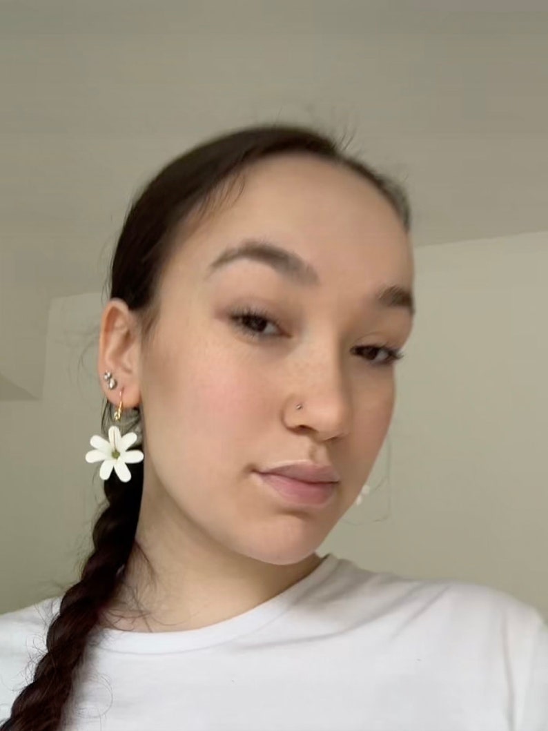 May include: White daisy flower earrings with gold-colored hoops. The earrings are a simple, elegant design, perfect for everyday wear. The earrings are lightweight and add a touch of nature-inspired charm.