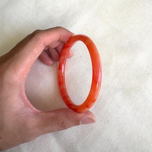 May include: A red jade bangle bracelet with white swirls. The bangle is smooth and polished.