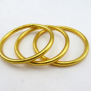 K&ouml;nnte beinhalten: Drei goldfarbene Metallarmreifen, die &uuml;bereinander gestapelt sind.
