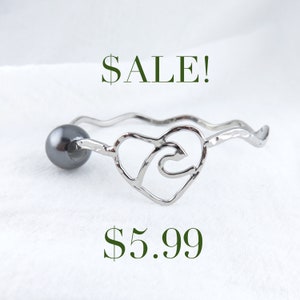 May include: Silver bracelet with a heart-shaped design and a black pearl accent. The bracelet is on sale for $5.99.