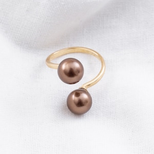 May include: A gold ring with two brown pearls. The ring is twisted and the pearls are positioned on either side of the twist.
